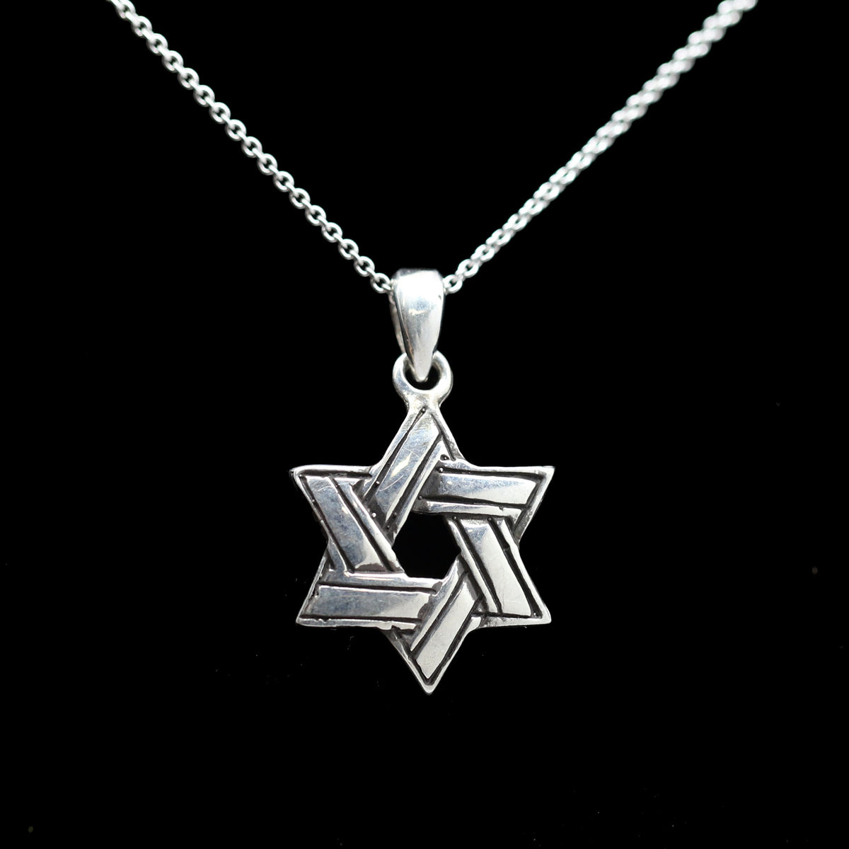 A sterling silver Star of David pendant necklace on a delicate silver chain, set against a solid black background.